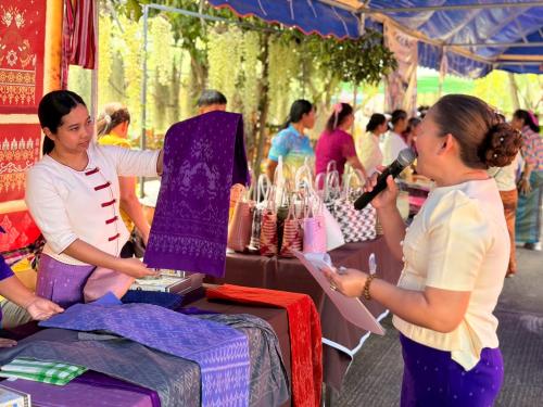 พิธีกรประจำงาน กำลังประชาสัมพันธ์ผ้าลายจักราชที่หน้าร้าน